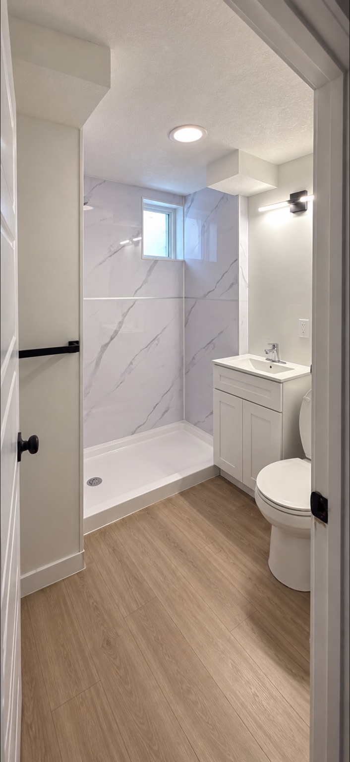 Completed bathroom with walk-in shower, vanity, and wood-look floor